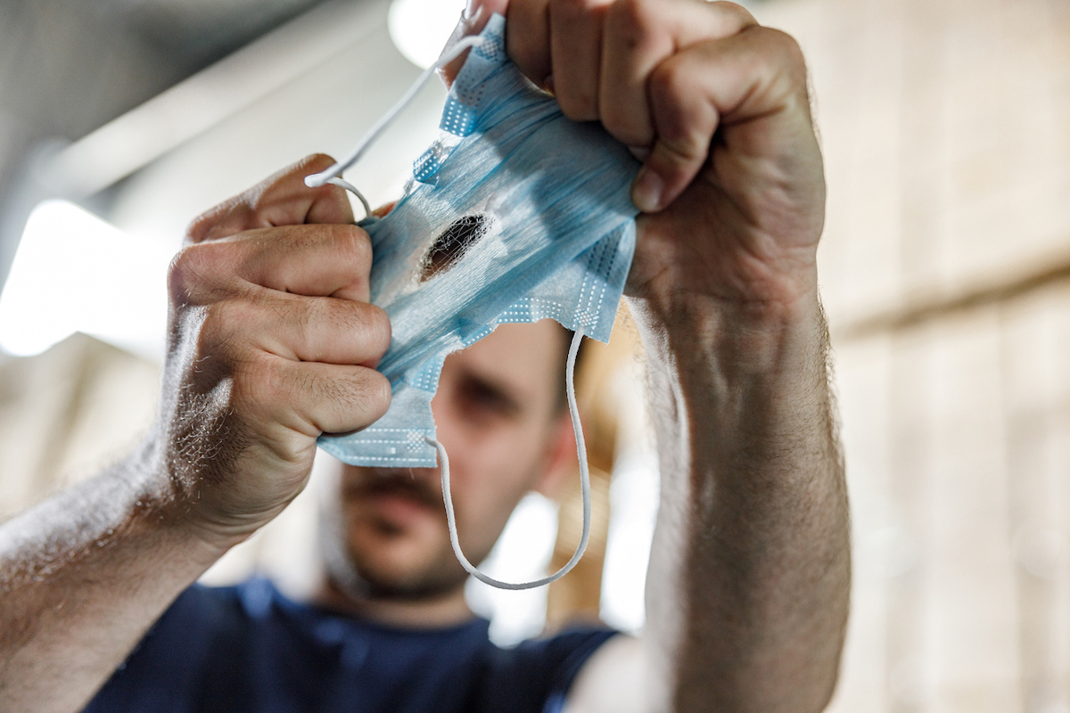 Man looking at hole in his protective face mask