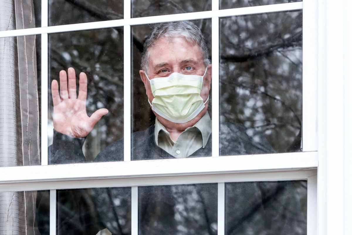 Man wearing mask with his hand up waving at the window