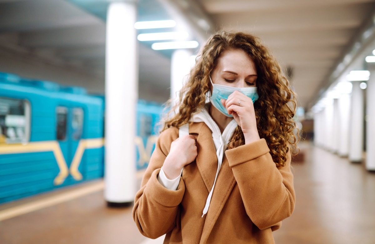 Woman coughing wearing a mask in subway station