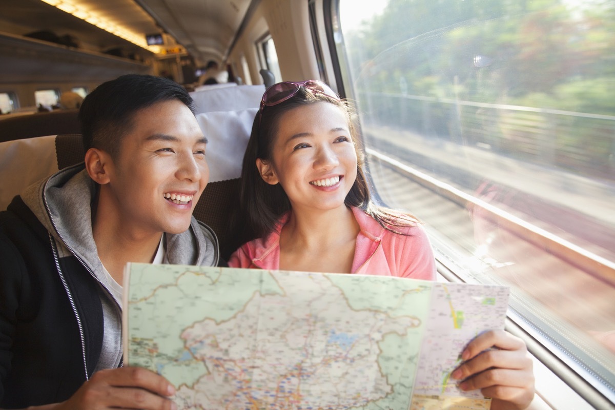 young asian man and young asian woman holding a map and looking out the window on a train