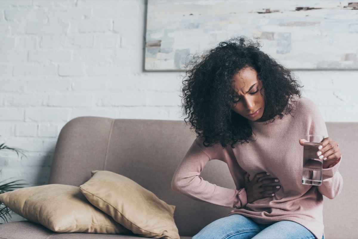 young woman holding glass of water with stomach pain