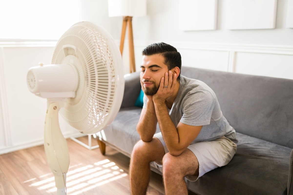 Happy young woman feeling better at home while relaxing in front of the electric fan during a bad heat wave