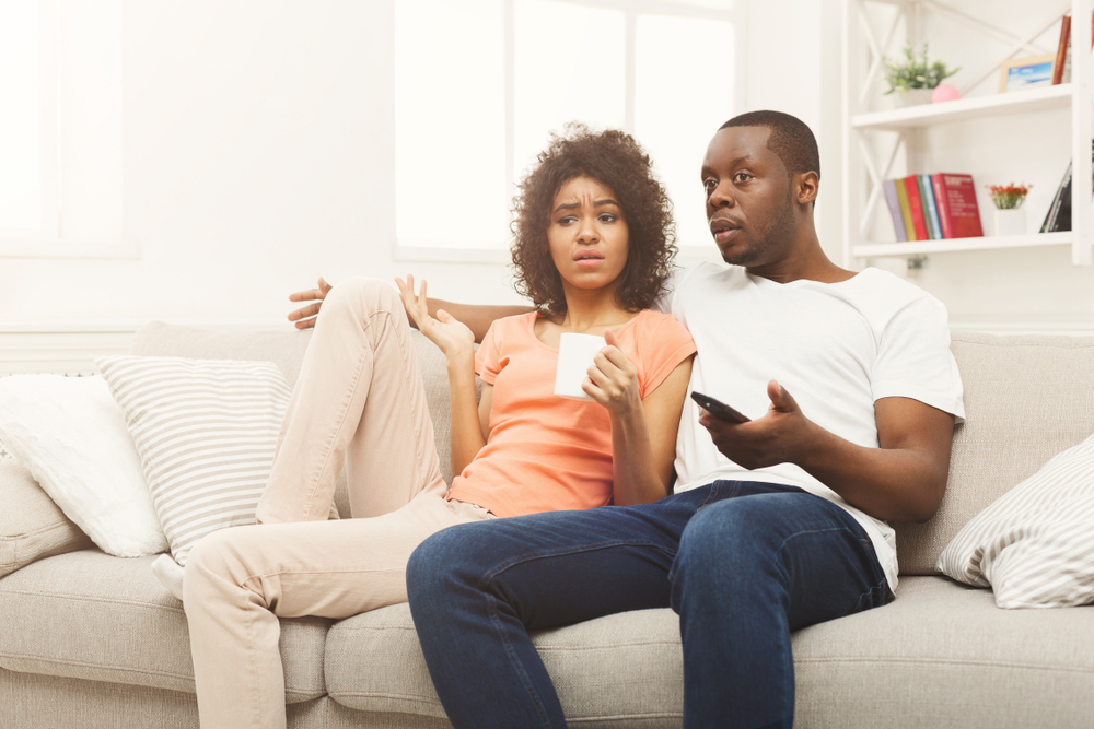 A young couple watching TV with a confused or disappointed look on their faces