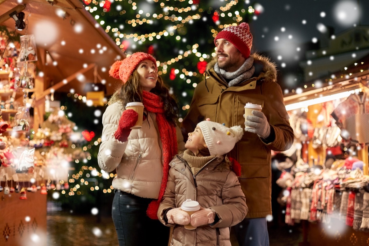 Man, woman, and little girl holding hot drinks and walking in Christmas market