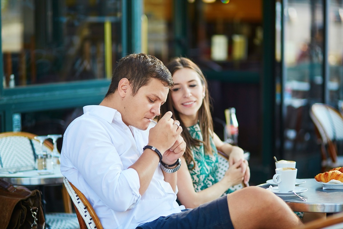 Young romantic couple drinking coffee, eating traditional French croissants and smoking in a cozy outdoor cafe in Paris, France