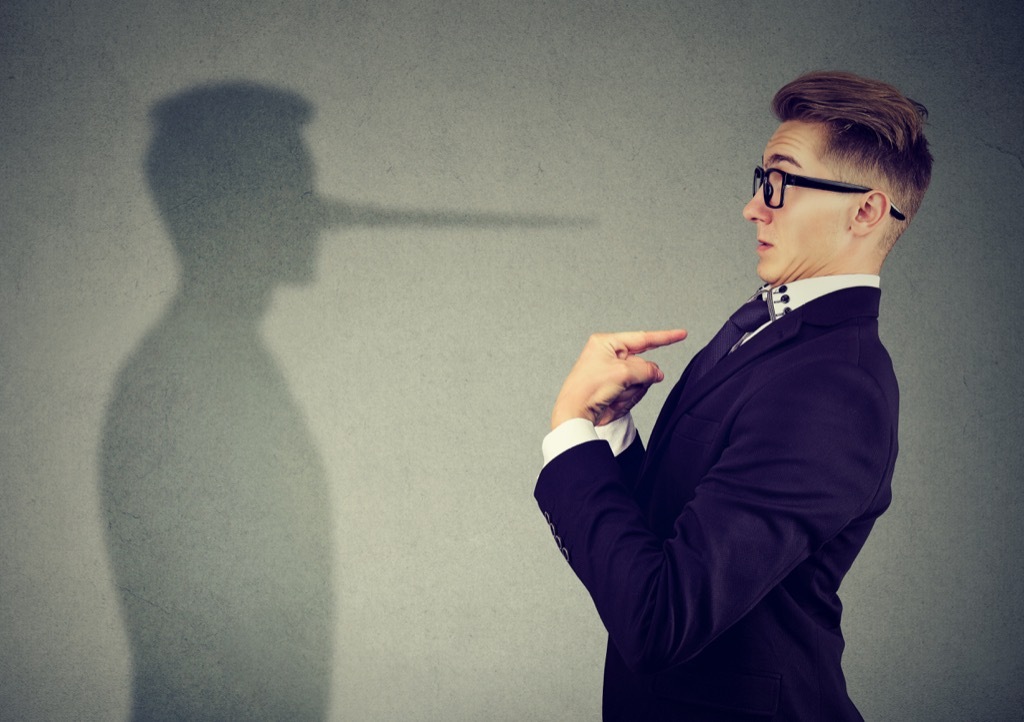 Man points finger at himself while his shadow shows a long nose, signs someone is lying