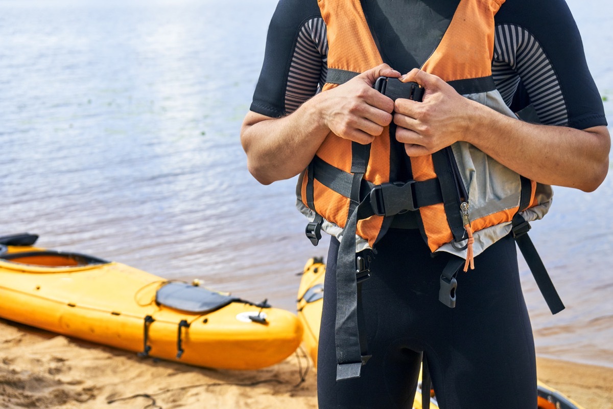 man connecting his life jacket together in front of a lake