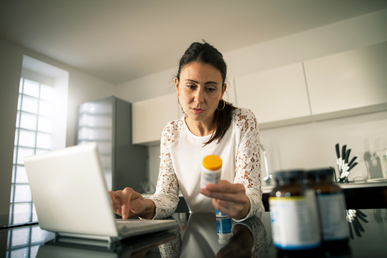 A woman sitting at her laptop and looking at a prescription pill bottle