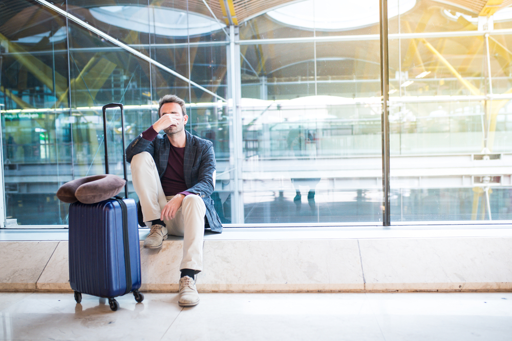 A man sitting in an airport with a distressed look on his face due to a delayed or cancelled flight