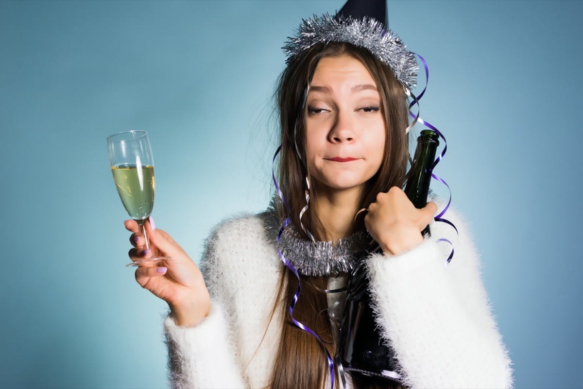 drunk woman in a festive cap holding champagne in hands