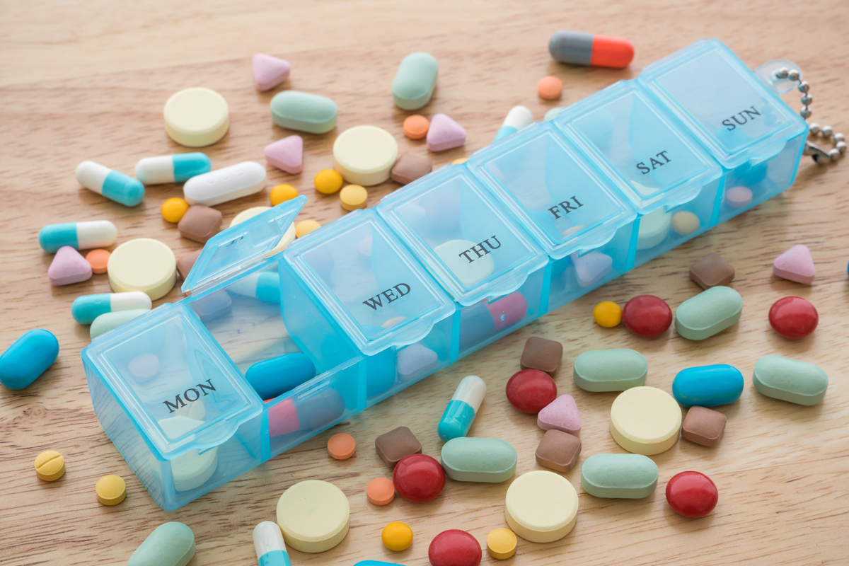 pill organizer with many different types of pills all over the table around it